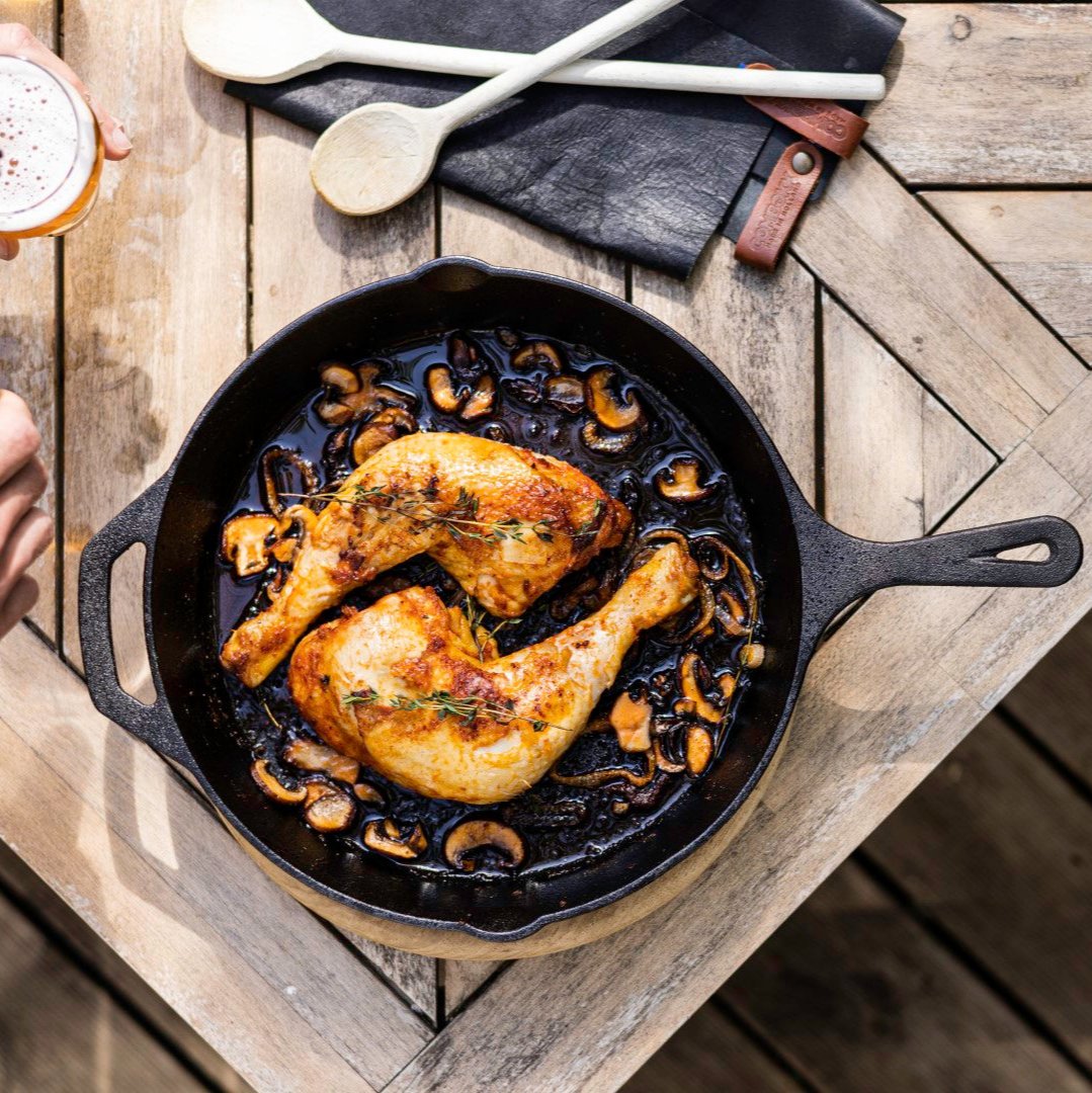 Een bovenaanzicht van een zware zwarte Kitchenz skillet gevuld met een sappige, goudbruin gebraden kip, omringd door gekleurde wortels en verse rozemarijn op een rustieke achtergrond. 
skillet met kip, Kitchenz gietijzeren braadpan, gebraden gevogelte in pan, eenpansgerecht gietijzer, Kitchenz culinaire fotografie, robuuste koekenpan met kipgerecht.